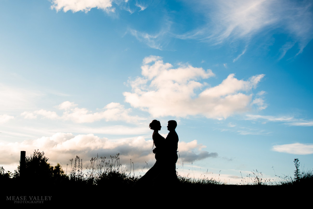 Photograph of bride and groom silhouetted against the sky on their wedding day.